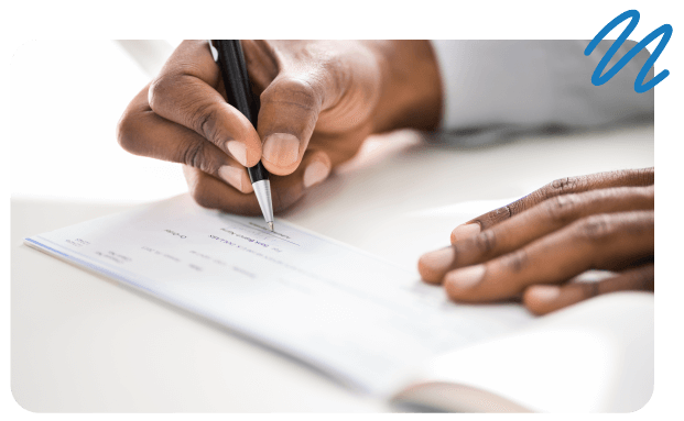 Person writing on check on table top.