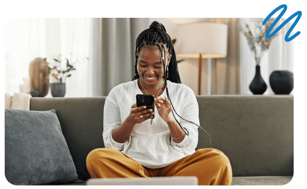 Girl sitting criss cross on couch looking at cell phone.