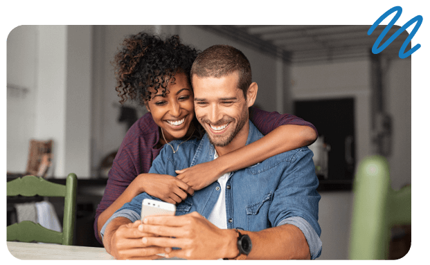 Woman with arms around man while both look at phone screen.