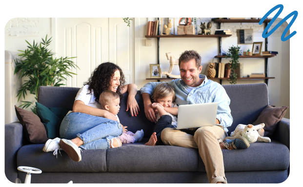 Family of four happy and sitting with one another on living room couch looking at laptop screen,