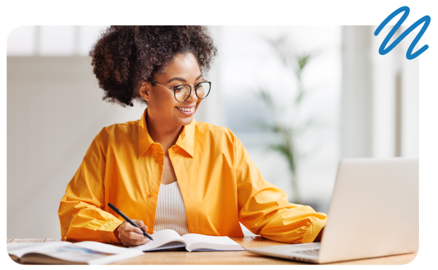 Smiling, happy woman with glasses working at desk with notebook and laptop.