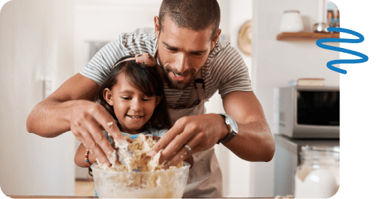 Father standing behind daughter mixing dough in bowl in kitchen.