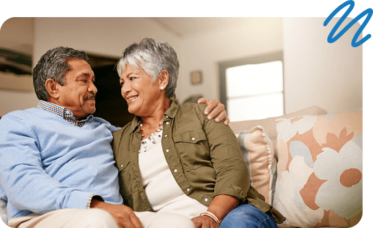 Couple staring happily at one another while sitting on couch in living room.