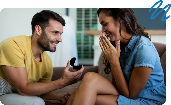 Man proposing to woman sitting on couch in living room.