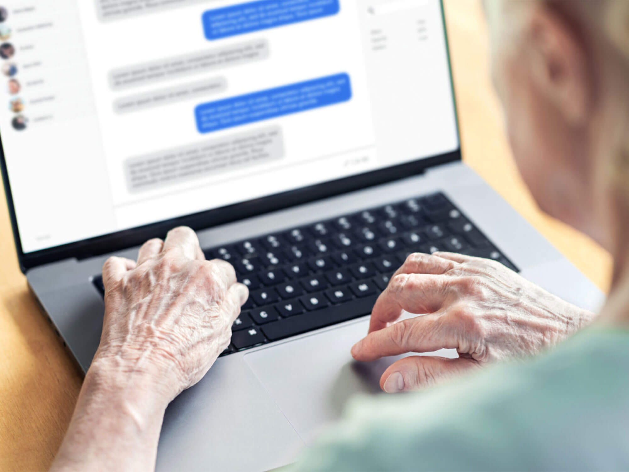 Elderly person using laptop with hands on keys and messages on screen.