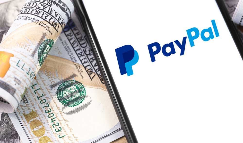 PayPal logo on the screen smartphone, and money, dollars. Paypal is an internet based digital money transfer service. Moscow, Russia - May 21, 2019